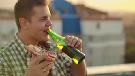 A-boy-eat-pieces-of-hot-pizza-and-drink-beer-on-the-roof.-He-smiles-and-enjoys-the-moment.